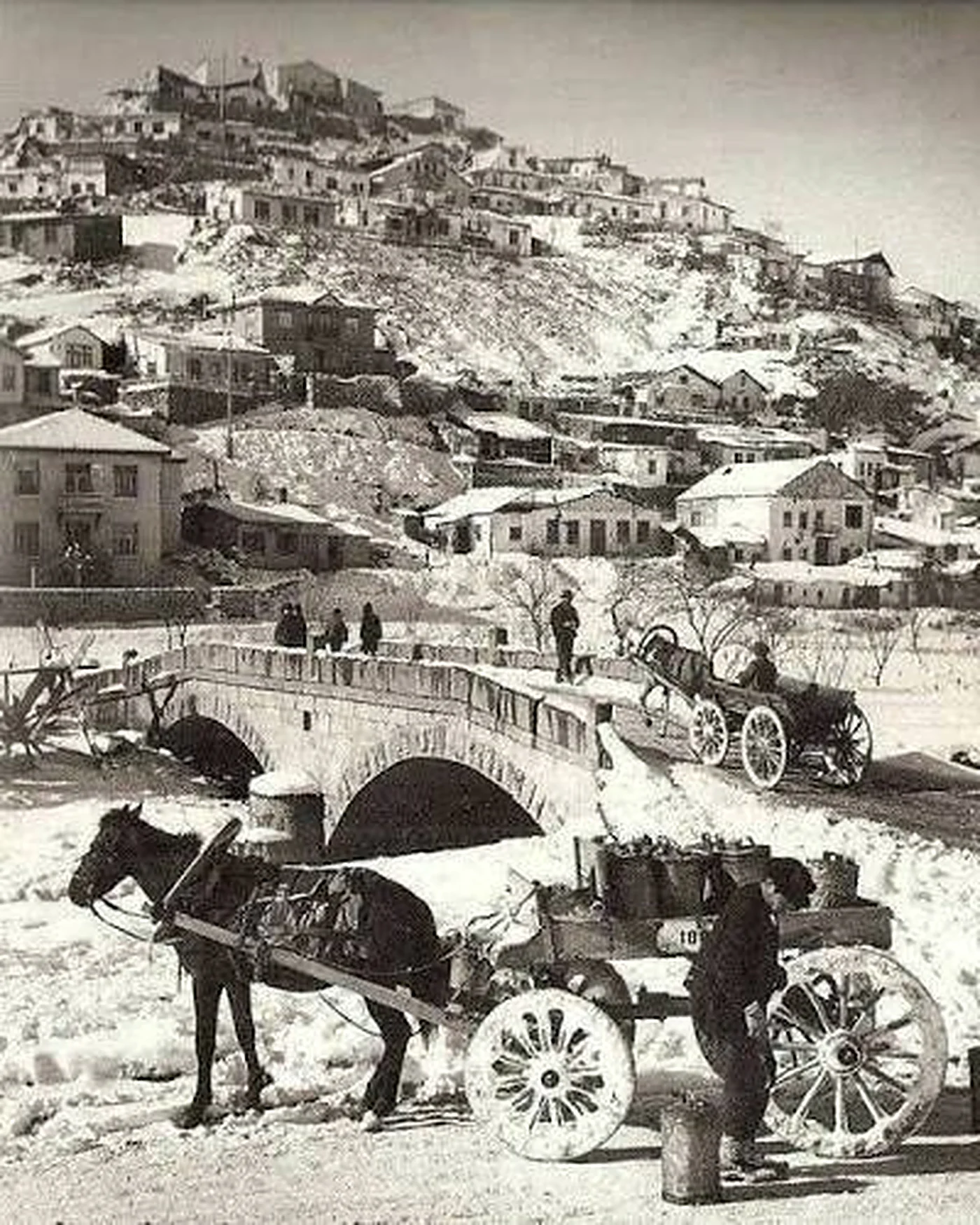 Eski bir Ankara fotoğrafı: karlı yamaçta evler, taş köprü ve atlı araba